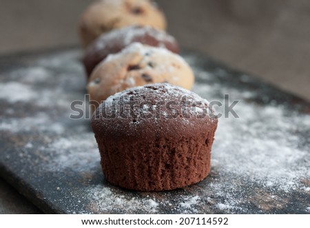 four chocolate and vanilla muffin on rustic bakery peel with sugar powder
