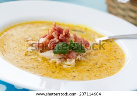 Indian soup Potage Mulligatawny with curry, bacon and basil in white soup bowl on blue desk with polka dot napkin