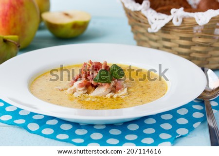 Indian soup Potage Mulligatawny with apple curry, bacon and basil in white soup bowl on blue desk with polka dot napkin
