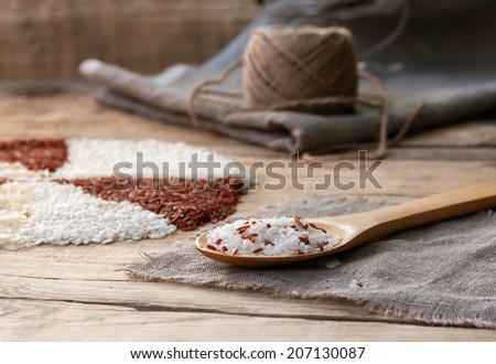 white and red rice in a wooden spoon on the sackcloth with ball of twine on an old wooden table
