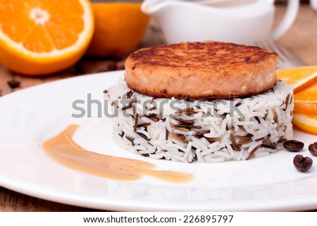 Salmon medallion with mixed cooked rice on white plate with coffee beans and orange. Wooden background