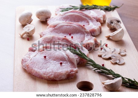 Pork tenderloin with champignon, rosemary, bay leaves, olive oil and pepper on wood cutting board.