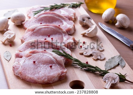 Pork tenderloin with champignon, rosemary, bay leaves, olive oil and pepper on wood cutting board.