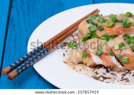 Chicken fillet served with miso sauce and rice on white plate. Wooden chopsticks. Blue wooden background.