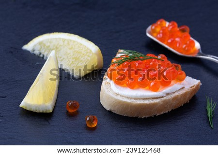 Bread with fresh cream cheese, red caviar and lemon on black slate plate