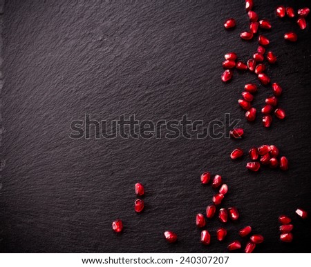 Ripe pomegranate seeds on rough black slate background. Copy space.