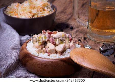 Chicken stew with rice, leek and bacon in wooden bowl. beer and bowl of Sauerkraut on rustic wooden desk