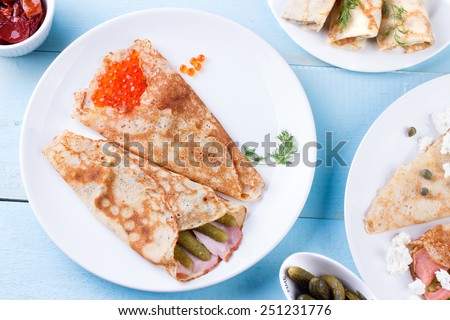 Pancake day, mardi gras, maslenitsa background. Thin rolled pancakes, crepes with red caviar and salmon, pickled cucumbers and bacon. Traditional Russian dish.