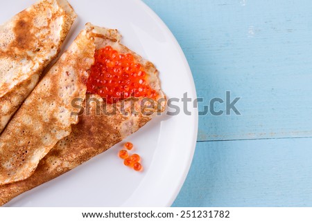 Pancake day, mardi gras, maslenitsa background. Thin rolled pancakes, crepes with red caviar. Traditional Russian dish.