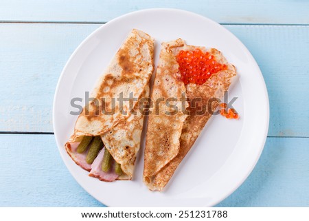 Pancake day, maslenitsa background. Thin rolled pancakes, crepes with red caviar, pickled cucumbers and bacon. Traditional Russian dish.