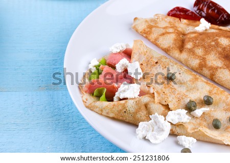 Pancake day, mardi gras, maslenitsa background. Thin rolled pancakes, crepes with salmon, feta cheese and dried tomatoes. Traditional Russian dish.