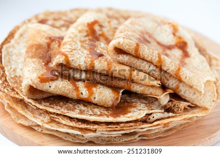 Thin pancakes, crepes with caramel syrup on round wooden  cutting board. Pancake day, maslenitsa background. Isolated.