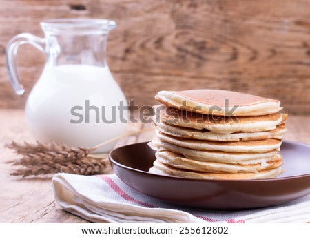 American pancakes with jug of milk on wooden background