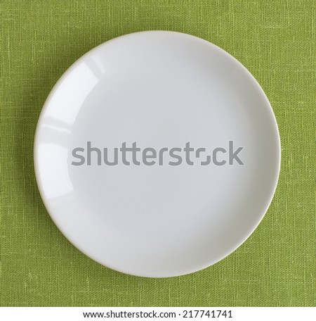 Blank white round ceramic plate isolated on background green linen tablecloth