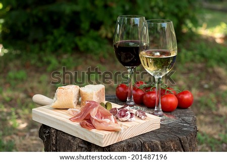 Red and white wine in a glass with sausage, ham and tomatoes in the nature. Selective focus on the wine