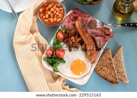Full English breakfast with baked beans, sausages, bacon. Selective focus on the egg and sausage.