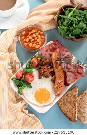 Full English breakfast with baked beans, sausages, bacon. Selective focus on the egg and sausage.