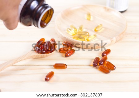 Closeup the yellow soft gelatin supplement fish oil capsule on wooden plate.