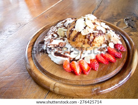 fresh cream puff with whipped cream and strawberries on wooden plate and brown wood table