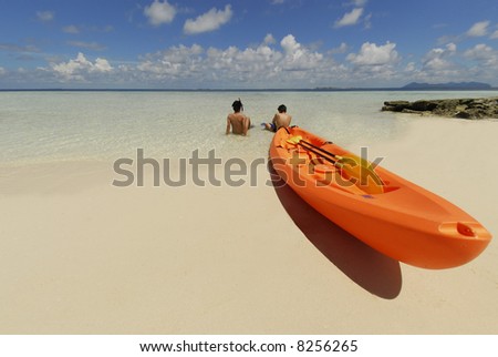 Two young men in a kayak under tropical sun surrounded by clean sands and blue seas.