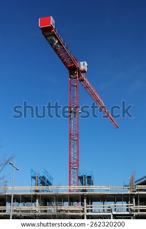 Construction site with red crane over a clean blue sky.