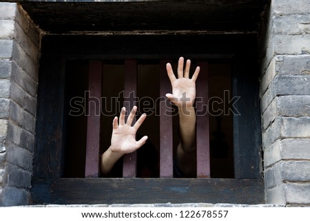 Prisoner hands stretch out from prison bars