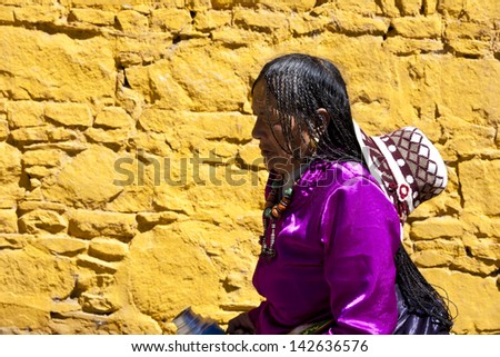 LHASA, TIBET-OCTOBER 07: A Tibetan woman wearing traditional clothes is passing a yellow wall st Sera Monastery on October 07, 2011 in Lhasa, Tibet.