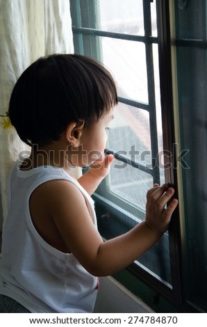 kid boy in a family sad standing near the house window, watching outside