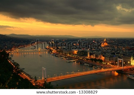 The beginnings of sunset in Budapest as the city lights come on, and car lights illuminate both the chain bridge and the Elizabeth bridge. The River Danube runs through the center of the frame.