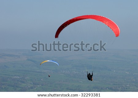 Two para-gliders above paragliding above a hazy landscape, enhancing the colors. One of the para-gliders happens to be in the distance, quite a way from the one that fills the frame.