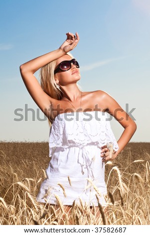 A woman in sun glasses stands in the field, wipes a forehead a right arm. Hard Light.