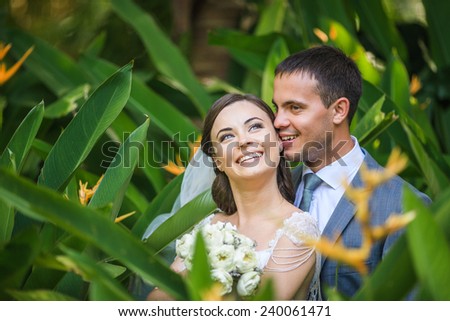 Groom is kissing his bride on the ear in a green leafy tropics