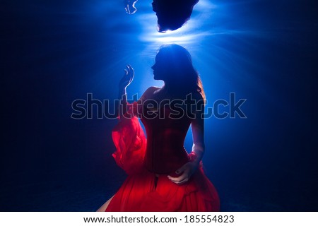 silhouette underwater photo pretty young girl  with dark long hair wearing red dress