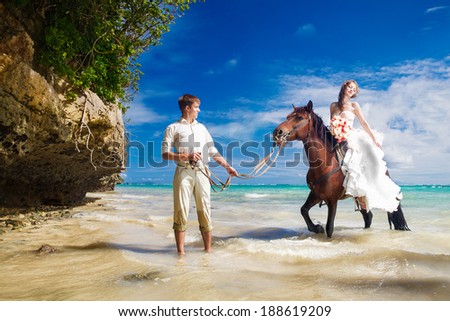 happy bride and groom walking with horse on a tropical beach