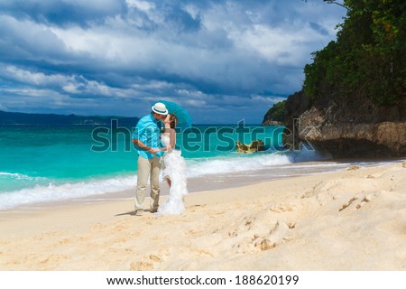 happy bride and groom with blue umbrella kiss on the tropical coast
