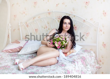 Beautiful young bride in a white dress with a wedding bouquet of pink roses lying on the bed in his bedroom. Last preparations for the wedding. The bride is waiting for the groom. Morning, the bride.