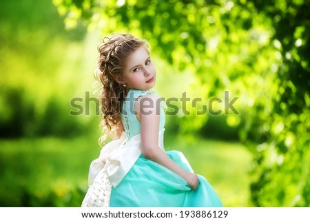 Beautiful little girl in a blue dress with a large white bow in spring garden. Little Princess.