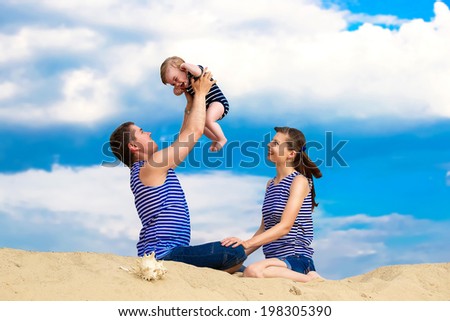 Happy family, mom, dad and little son in striped vests having fun  in the sand outdoors against blue sky background. Summer vacations concept.