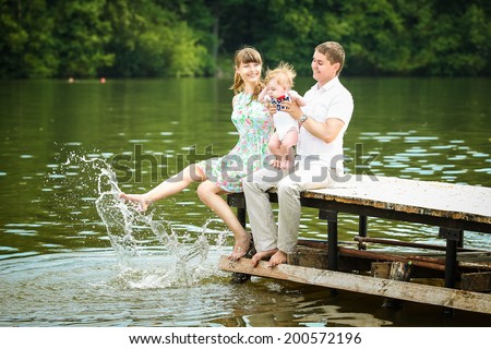 Happy family, mom, dad and little son having fun in the park on the lake shore background. Summer vacations concept.