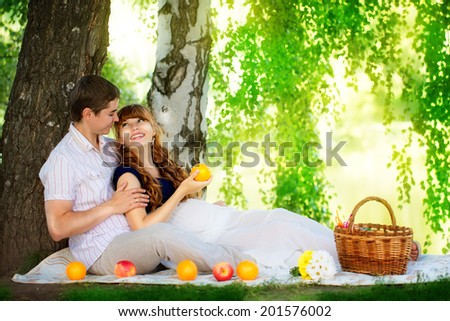 Happy and young pregnant couple hugging in nature enjoying summer park, outdoors, new life concept.