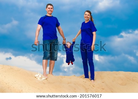 Happy family, mom, dad and little son having fun  in the sand outdoors against blue sky background. Summer vacations concept.