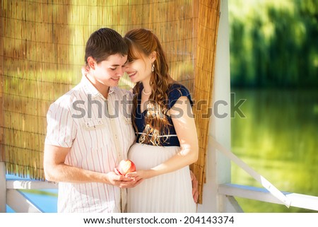 Happy and young pregnant couple hugging in the park. Summer vacation. New life concept. Future mother and father.
