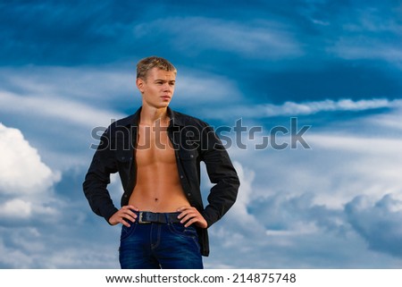 Young handsome man on the beach. Looks thoughtfully into the distance. The sky in the background. Summer vacation concept.