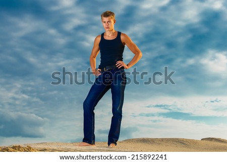 Young handsome man on the beach. Looks thoughtfully into the distance. The sky in the background. Summer vacation concept.