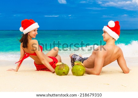 Young beautiful couple in love having fun in the waves dressed in red Santa Claus hats. Christmas and New Year on the tropical coast.