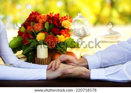 Women\'s and men\'s hands with wedding rings at a table decorated for a romantic dinner.