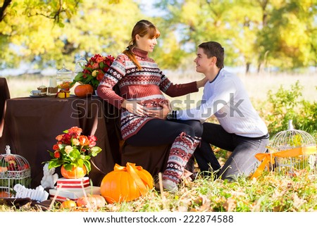Beautiful Young Pregnant Couple Having Picnic in autumn Park. Happy Family Outdoor. Smiling Man and Woman relaxing in Park. Relationships.