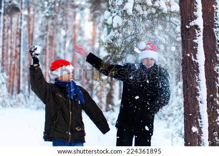 Two teenagers in Christmas hats Santa Claus having fun in the snow-covered forest playing in the snow.