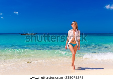 Young beautiful girl in wet white shirt  on the beach. Blue tropical sea in the background.