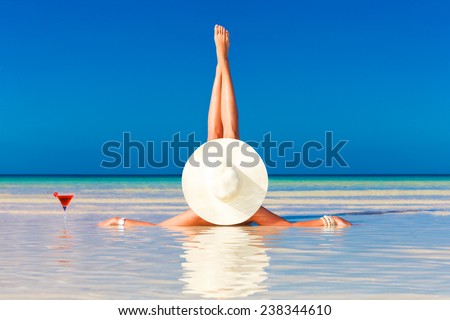 young woman in straw hat laying at the tropical beach and enjoying cocktail